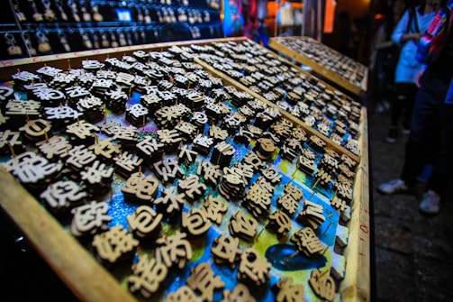 An array of wooden blocks with engraved Chinese characters, likely used for printing or stamping. The scene is vibrant, with an array of blocks neatly arranged on trays, surrounded by dim lighting. There's a focus on the intricate detail of the characters, each one carefully crafted.