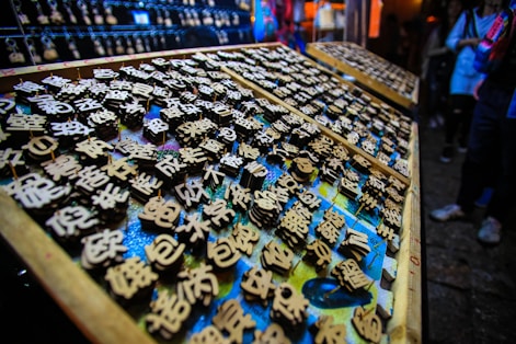 An array of wooden blocks with engraved Chinese characters, likely used for printing or stamping. The scene is vibrant, with an array of blocks neatly arranged on trays, surrounded by dim lighting. There's a focus on the intricate detail of the characters, each one carefully crafted.