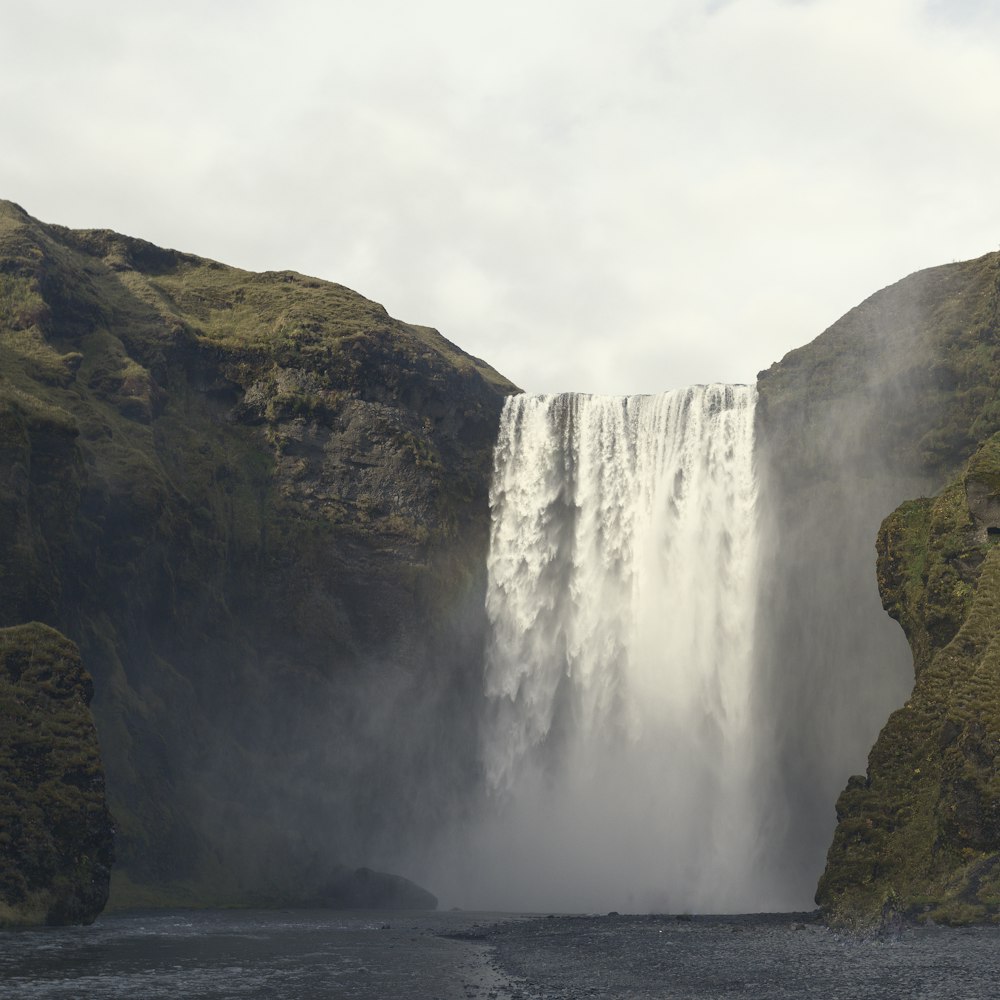 waterfalls between green mountains under cloudy sky