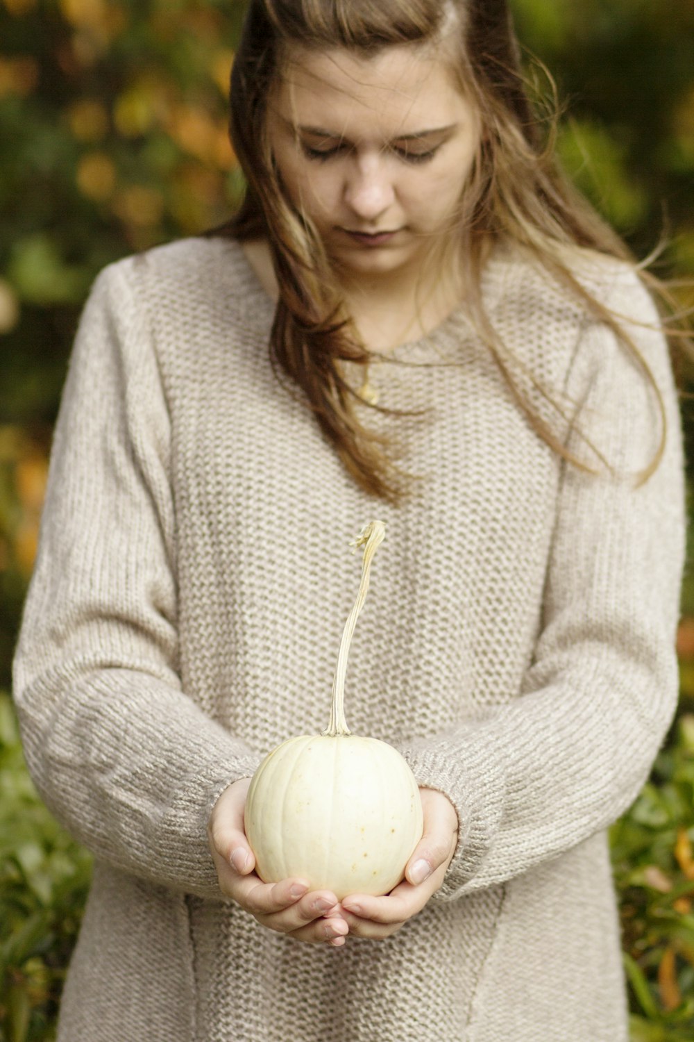 a woman holding a white pumpkin in her hands