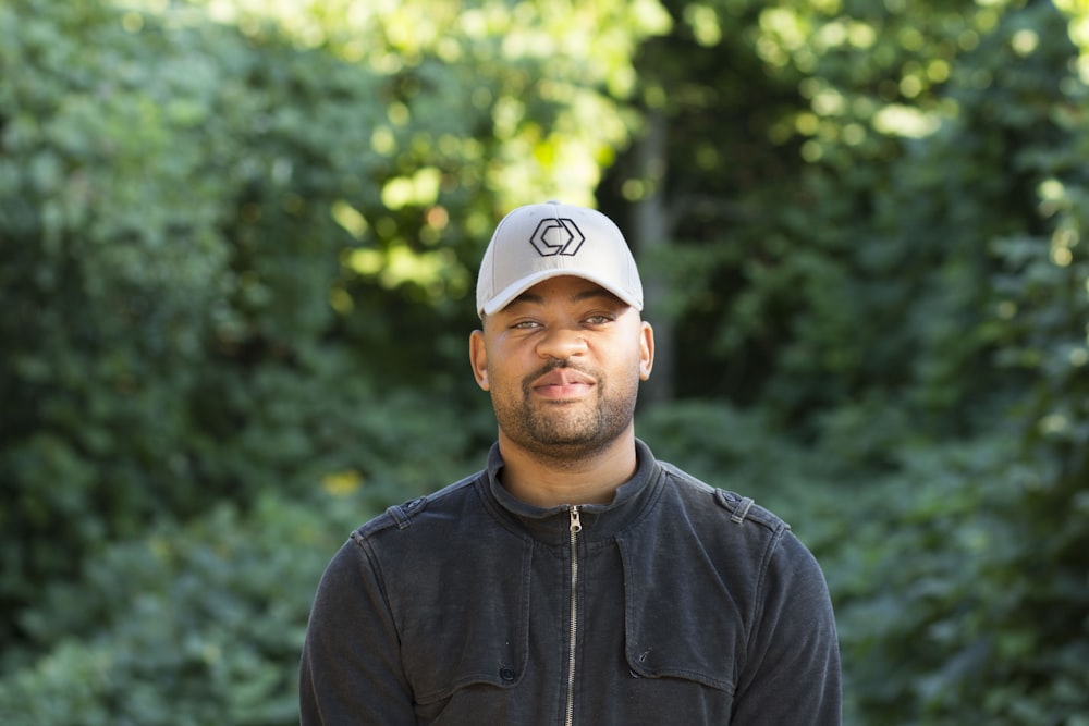 a man wearing a baseball cap standing in front of trees