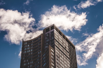 A modern high-rise building with a curved facade set against a backdrop of a vibrant blue sky filled with fluffy white clouds.