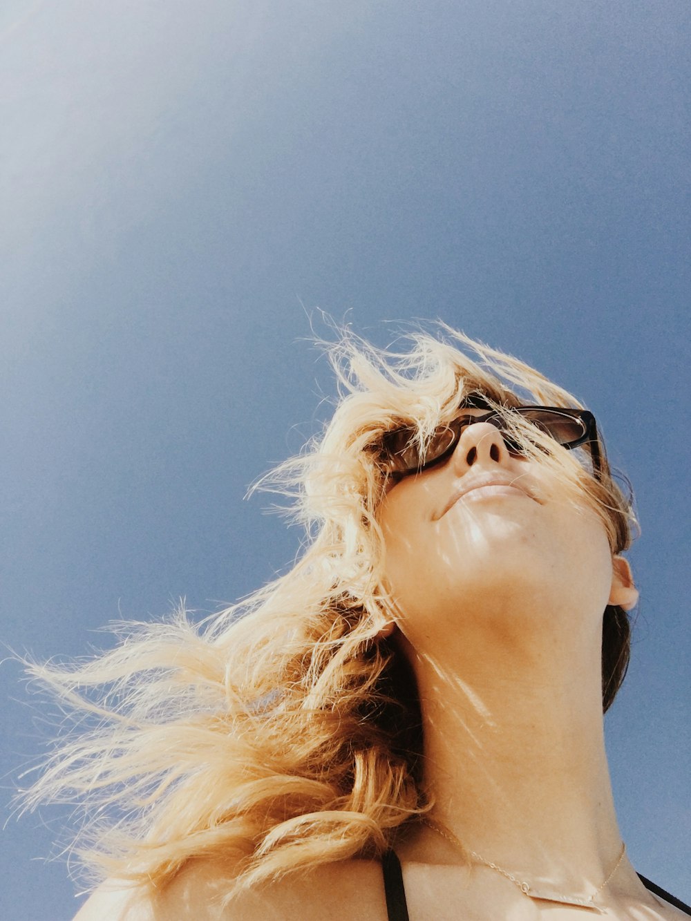 A happy blonde girl wearing glasses outside.