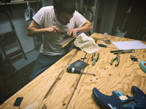 Close-up of a skilled guitar technician adjusting the tuning pegs on an electric guitar in a cozy workshop.