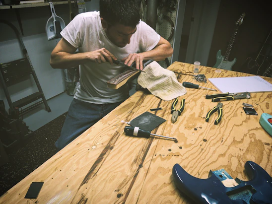 A skilled luthier carefully repairing a guitar in a cozy workshop filled with various musical instruments.