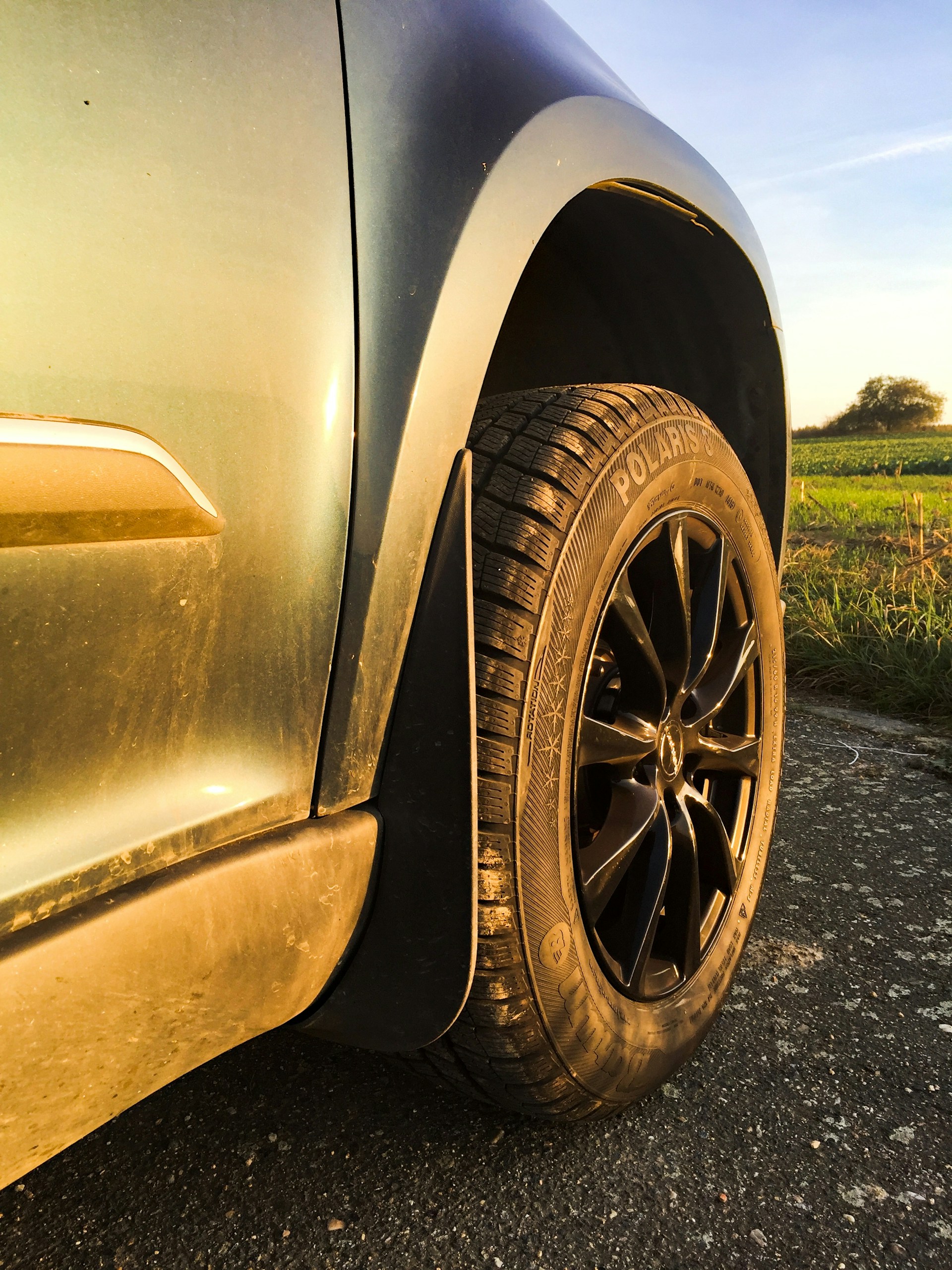 A close-up of a car's wheel rolling smoothly on a quiet country road surrounded by lush greenery and sunshine.