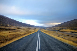 landscape photography of black asphalt road with white line surrounded by brown grass field during daytime