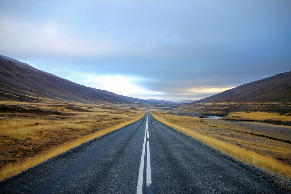 Fotografia de paisagem de estrada de asfalto preto com linha branca cercada por campo de grama marrom durante o dia