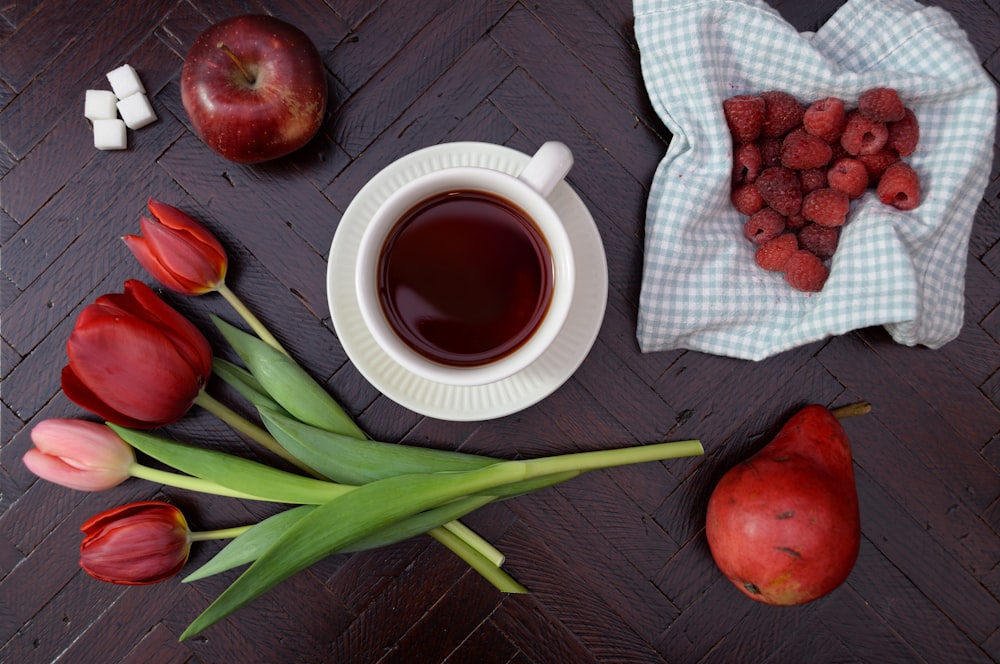 tazza da tè su piattino vicino al melo e al fiore di tulipano