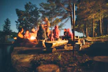 Campfire gathering at dusk with people sharing stories and laughter in the woods.