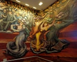 A vibrant mural depicting stylized figures in motion. People are dressed in early 20th-century attire, characterized by top hats and elaborate gowns. The composition features dynamic lines and exaggerated forms, suggesting movement and energy.