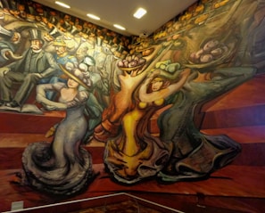 A vibrant mural depicting stylized figures in motion. People are dressed in early 20th-century attire, characterized by top hats and elaborate gowns. The composition features dynamic lines and exaggerated forms, suggesting movement and energy.