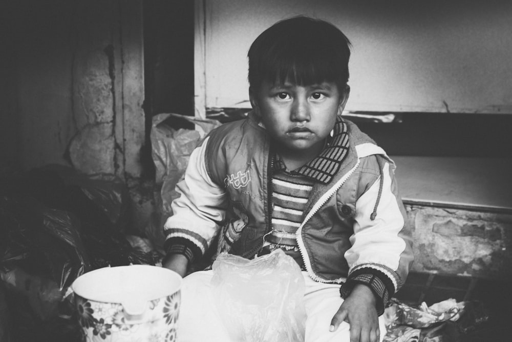 grayscale photo of boy in jacket holding white plastic bag