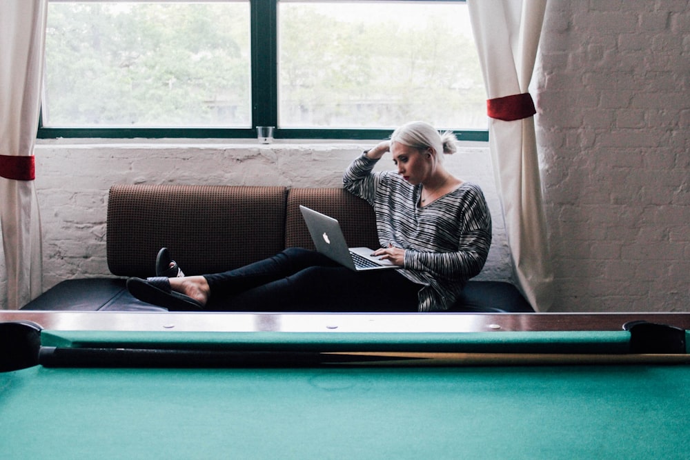 woman sitting on sofa holding silver MacBook