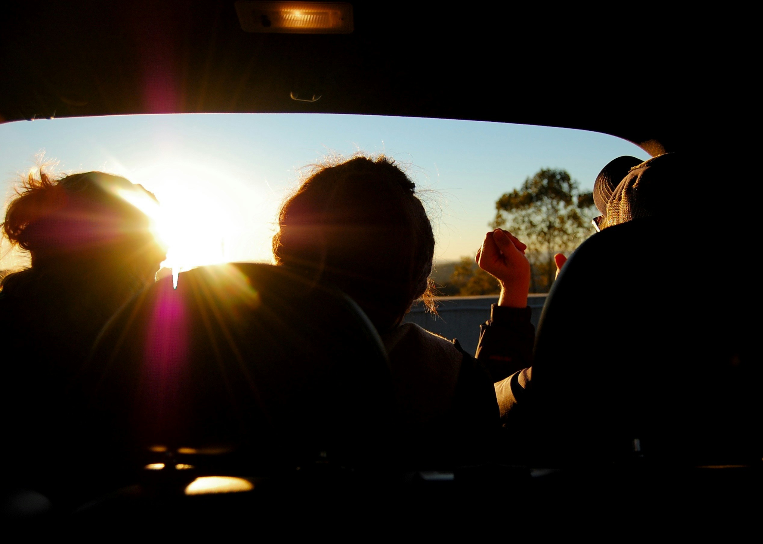 Three silhouettes watching sunset from a car