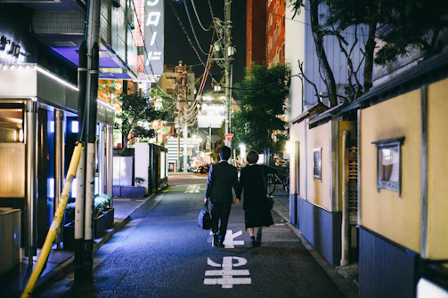 Couple walking hand in hand through a softly lit urban street at dusk.