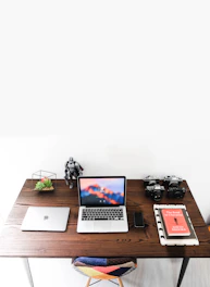 Modern electronics and marketing books stacked neatly on a desk with a matte forest green background.