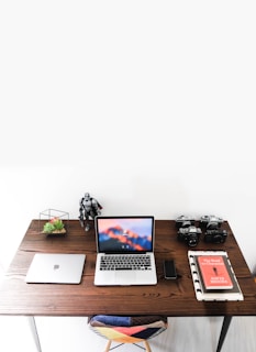 An organized desk with a white background, a laptop, and a bonsai tree casting gentle shadows.