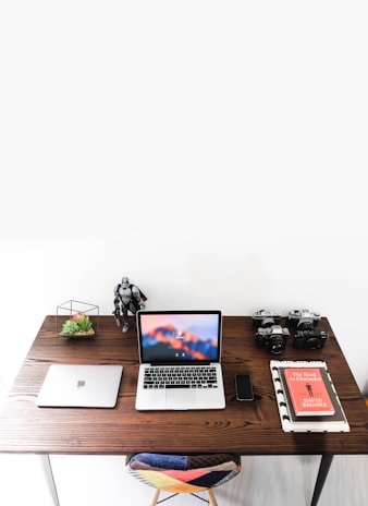 An organized desk with a white background, a laptop, and a bonsai tree casting gentle shadows.
