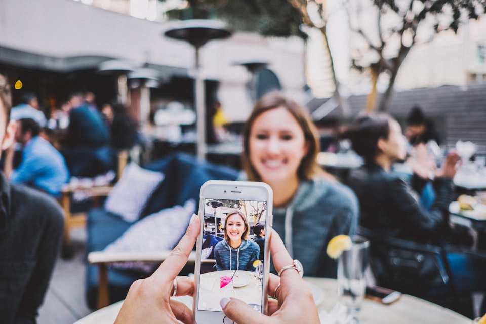 Close-up view of a person's hands and white iPhone taking a picture of a smiling woman.