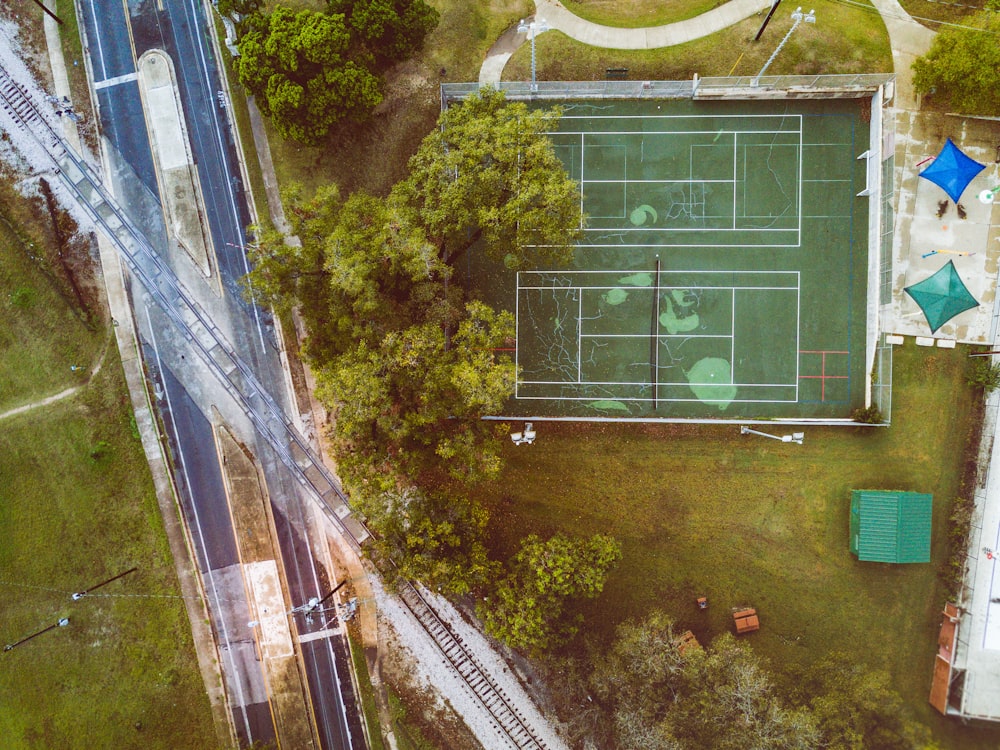 높은 각도 사진 녹색 잔디 테니스 코트 근처 나무, 도로, 및 철도