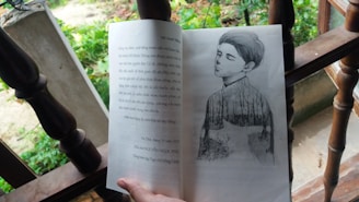 An open book resting on a wooden surface features an illustration of a contemplative figure with closed eyes, blended with a nature scene. The background suggests an outdoor setting with greenery and leaves.