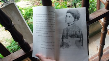 An open book resting on a wooden surface features an illustration of a contemplative figure with closed eyes, blended with a nature scene. The background suggests an outdoor setting with greenery and leaves.