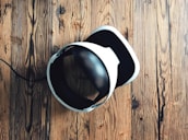 A virtual reality headset with a sleek design rests on a rustic wooden surface, creating a contrast between modern technology and natural textures. The headset is mainly black and white.