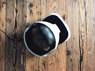 A virtual reality headset with a sleek design rests on a rustic wooden surface, creating a contrast between modern technology and natural textures. The headset is mainly black and white.
