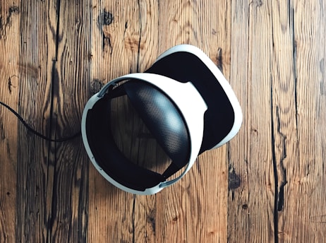 A virtual reality headset with a sleek design rests on a rustic wooden surface, creating a contrast between modern technology and natural textures. The headset is mainly black and white.