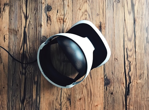 A virtual reality headset with a sleek design rests on a rustic wooden surface, creating a contrast between modern technology and natural textures. The headset is mainly black and white.
