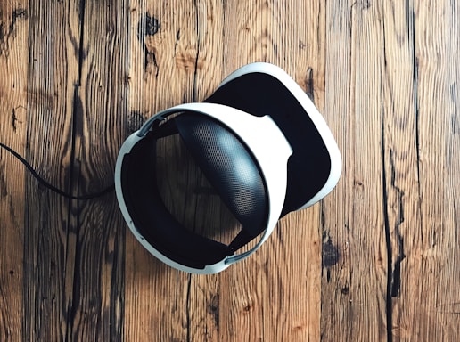 A virtual reality headset with a sleek design rests on a rustic wooden surface, creating a contrast between modern technology and natural textures. The headset is mainly black and white.