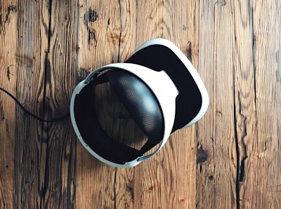 A virtual reality headset with a sleek design rests on a rustic wooden surface, creating a contrast between modern technology and natural textures. The headset is mainly black and white.
