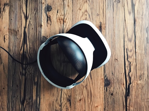 A virtual reality headset with a sleek design rests on a rustic wooden surface, creating a contrast between modern technology and natural textures. The headset is mainly black and white.