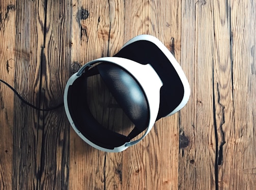 A virtual reality headset with a sleek design rests on a rustic wooden surface, creating a contrast between modern technology and natural textures. The headset is mainly black and white.