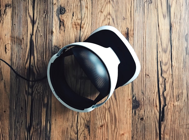 A virtual reality headset with a sleek design rests on a rustic wooden surface, creating a contrast between modern technology and natural textures. The headset is mainly black and white.