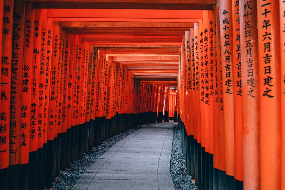 An orange walkway path with consistent architecture at Fushimi inari Trail leading to the shrine