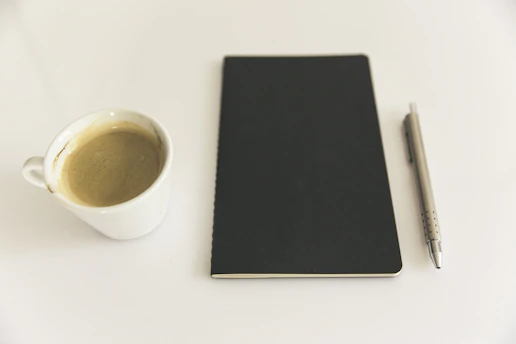 Minimalist design showing a clean desk with a notebook, pen, and a cup of coffee.