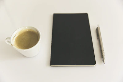 A calm, minimalist workspace with a notebook open to handwritten notes and a simple coffee cup beside it.