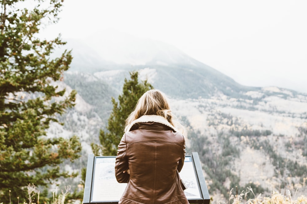 back photo of woman wearing black leather jacket in front of snowed mountain