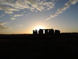 Sunlight casting long shadows over a circle of towering stone monoliths at dawn.