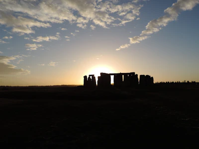 Sunlight casting long shadows over a circle of towering stone monoliths at dawn.