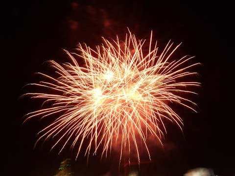 Bright, colorful display of fireworks against a dark night sky with bursts of orange and white sparks radiating outward.