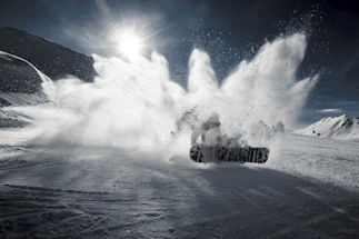 A dynamic snowscoot rider catching air against a snowy mountain backdrop at sunset.