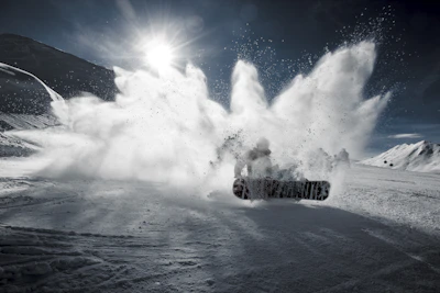 A snowscoot rider launching off a snowy mountain jump with dramatic alpine peaks behind.