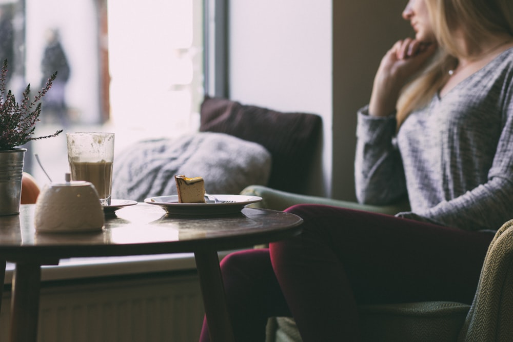 mujer con camisa gris de manga larga frente a la mesa con un pedazo de pastel