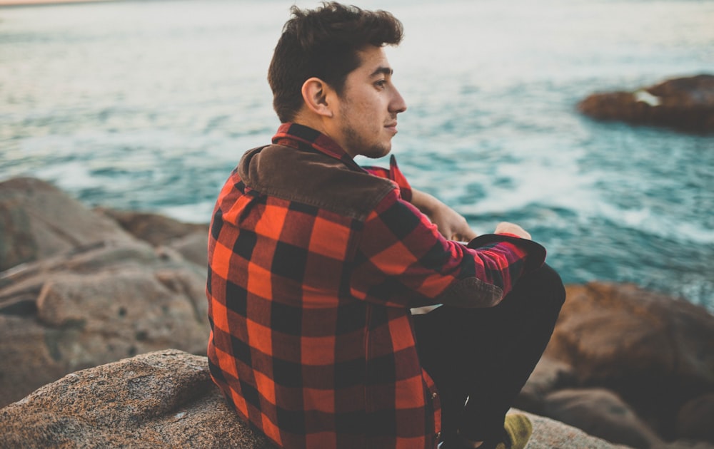 man sitting boulder near body of water