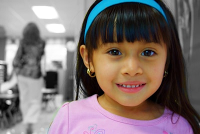 Soft-focus photo of a little girl smiling shyly while wearing a delicate headband.