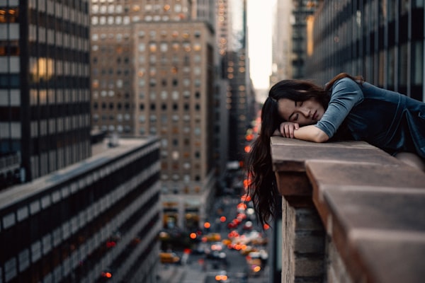 a woman leaning on the ledge of a building in a city