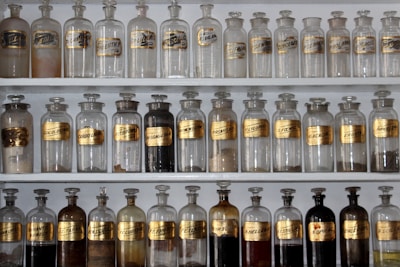 Delicate glass bottles filled with herbal tinctures arranged on a white shelf with natural light.